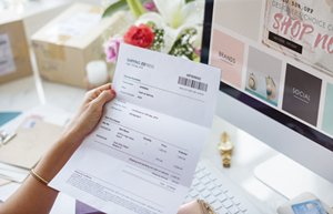 Bildausschnitt mit einer Rechnung, von einer Frauenhand gehalten, vor einem Webshopwebseite